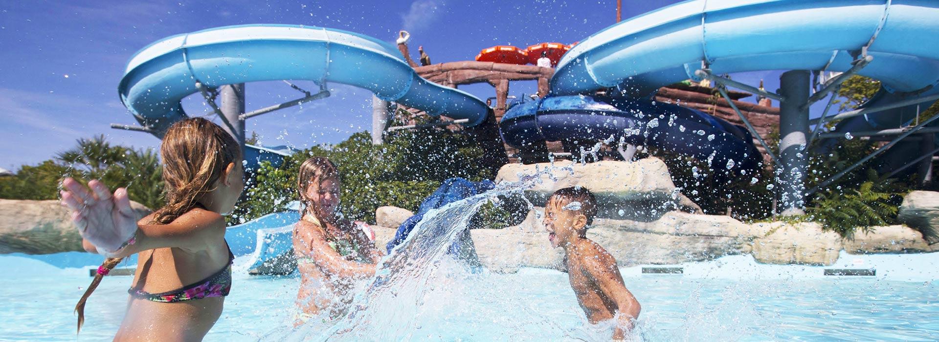Bambini giocano felici in piscina con scivoli d'acqua.
