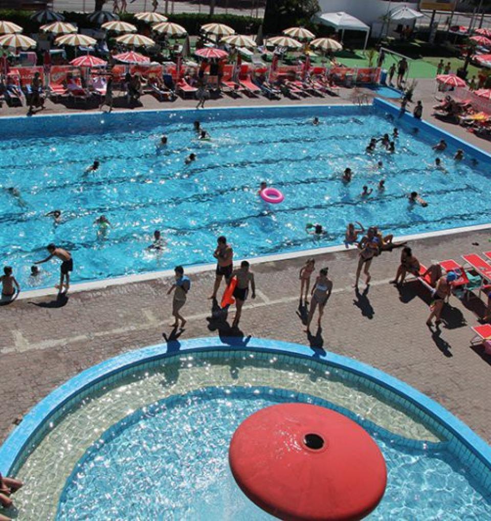 Piscina affollata con ombrelloni colorati e persone che nuotano.