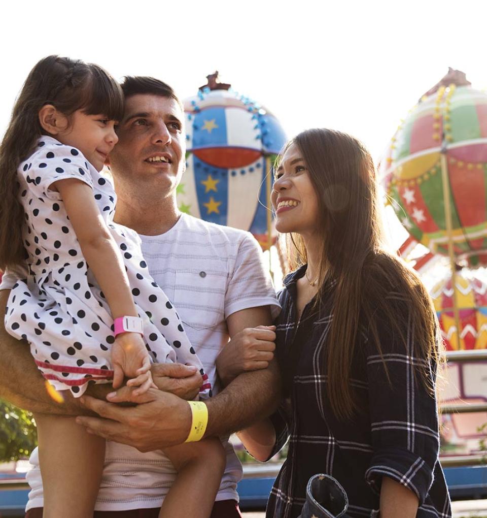 Famiglia felice in un parco divertimenti con giostre colorate sullo sfondo.